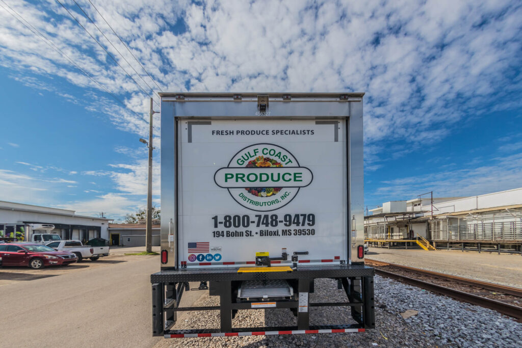 The back of a delivery truck with the Gulf Coast Produce Distributors Inc. logo and the words "1-800-748-9479 194 Bohn St. Biloxi, MS 39530"